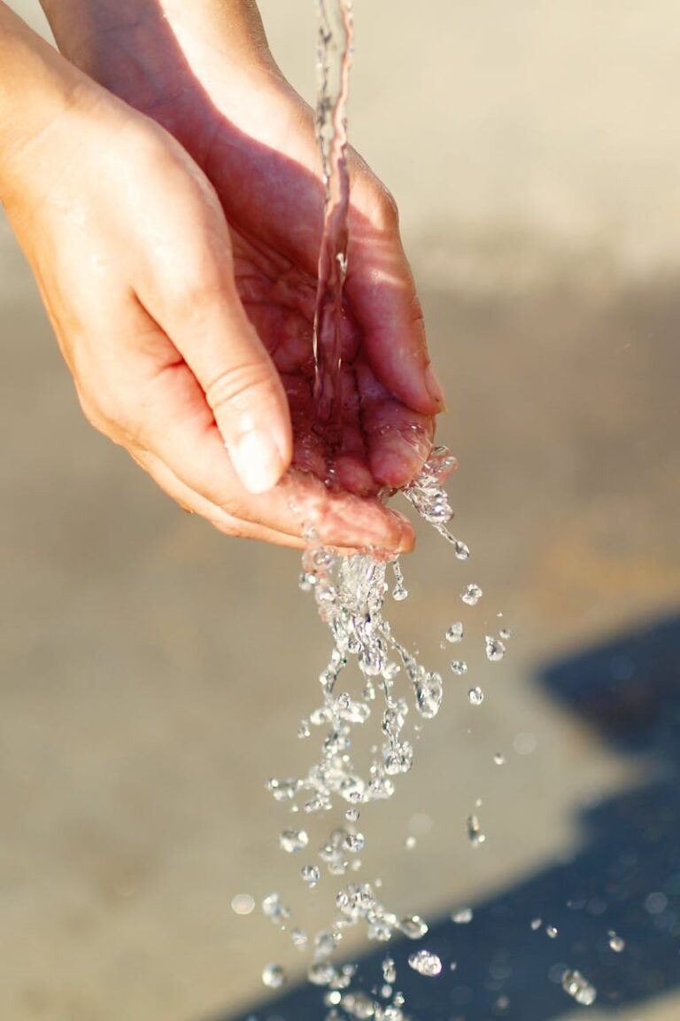 Close-up of hands catching flowing water outdoors, symbolizing freshness and purity.